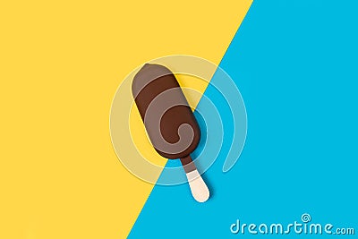 Dark chocolate dipped ice lolly on a yellow and light blue background Stock Photo