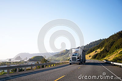 Dark classic semi truck with trailer driving on highway along th Stock Photo