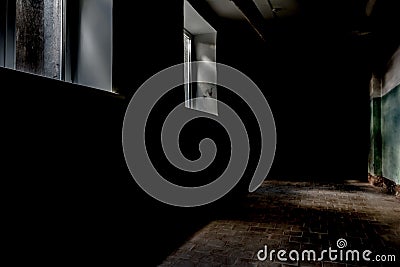 A dark corridor with two rectangular windows, dim daylight illuminates a part of the wall and the floor surface with a tile Stock Photo