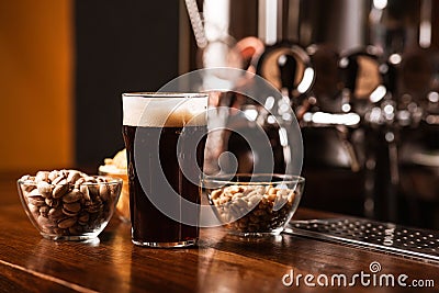 Dark craft beer with snacks. Near are pistachios, chips and nuts in plates and dark beer with foam Stock Photo
