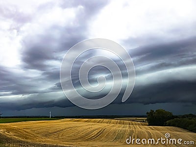 Dark cumulonimbus clouds bringing heavy rain over harvested agrarian fields Stock Photo