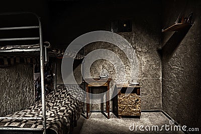 Dark empty jail cell with iron bunk bed and wooden bedside table Stock Photo