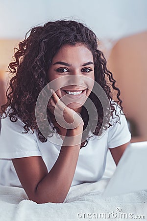 Dark-eyed curly girl smiling while watching photos Stock Photo