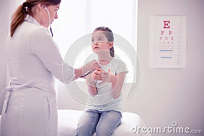 Dark-eyed little girl feeling calm while sitting in front of family physician Stock Photo