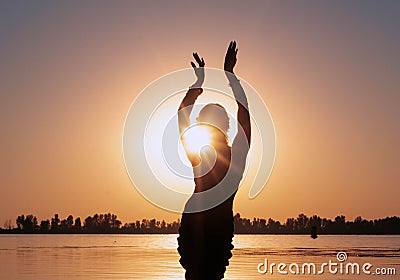 Dark glowing silhouette of slim woman with hands up near big river Stock Photo