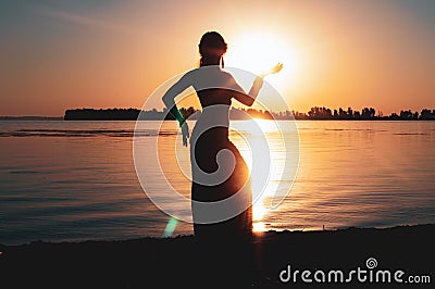 Silhouette of slim woman illuminated with sunshine in front of red aurora sky Stock Photo