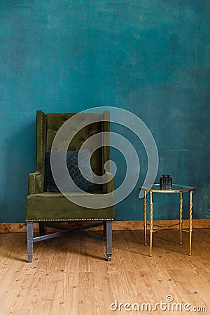 Dark green soft armchair near plaster wall. Stock Photo