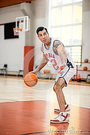 Dark-haired athletic man playing basket-ball in the gym Stock Photo