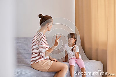 Dark haired female with hair bun speech pathologist having lesson with little girl, training pronunciation of sounds and Stock Photo