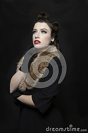 A dark-haired 1940s young woman wearing a black vintage coat dress and a fur collar Stock Photo