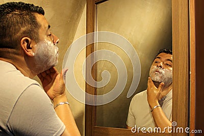 Dark-haired 40-year-old Latino man does his beauty routine, shaves with shaving cream and soap to avoid folliculitis Stock Photo