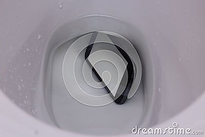 Dark phone fell in water in a toilet bowl, the top view, phone lies under water with reflection of walls of a toilet bowl Stock Photo