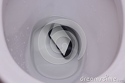 Dark phone fell in water in a toilet bowl, the top view, phone lies under water with reflection of walls of a toilet bowl Stock Photo