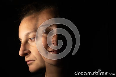 Dark portrait of a smiling woman with only half her face lit up on a black background that unfolds into another blurred face with Stock Photo