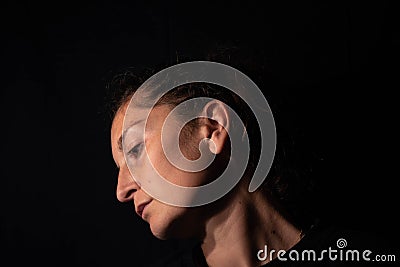 Dark profile portrait of a very dimly lit woman. The woman is looking sideways conveying a feeling of sadness or abandonment Stock Photo