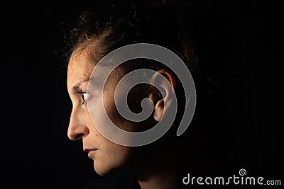 Dark profile portrait of a very dimly lit woman. The woman is looking straight ahead and transmits sadness or depression Stock Photo