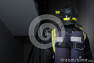 In a dark room, close-up of the back of a firefighter in protective clothing and a helmet with a flashlight Stock Photo