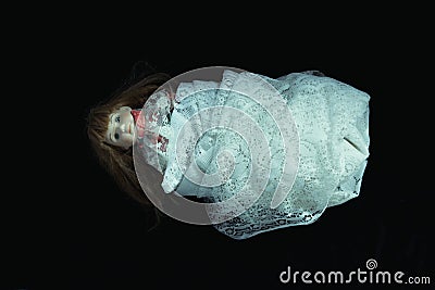 A dark, scary edit of an old doll wrapped in a white net curtain on a black background Stock Photo