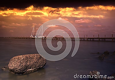 Dark shot nit dramatic sky of a lake with a long jetty and a ship in the background Stock Photo