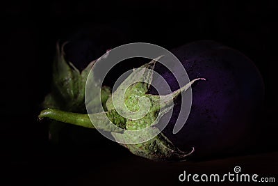 Dark shot of two purple aubergines with green stems lying side by side against a dark background Stock Photo