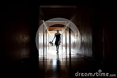 A dark silhouette of a child with a Teddy bear. One child with a dark long corridor. Spooky scary hallway. The house is haunted. Stock Photo