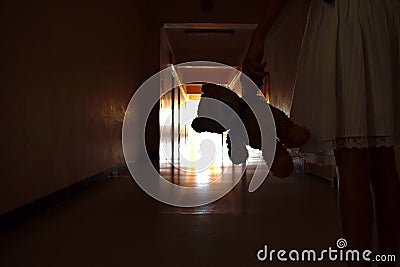 A dark silhouette of a child with a Teddy bear. One child with a dark long corridor. Spooky scary hallway. The house is haunted. Stock Photo