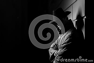 Dark silhouette of a man in a raincoat with a hat at night Stock Photo