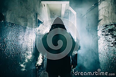 Dark silhouette of strange danger man in hood in back light with smoke or fog in scary grunge corridor or tunnel Stock Photo