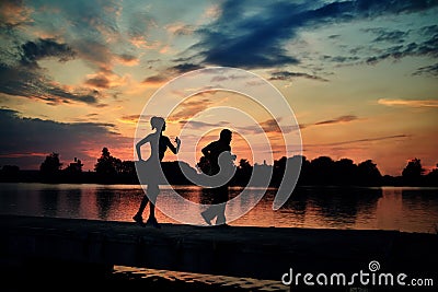 Dark silhouettes of scamper runners while sunset near lake. Stock Photo