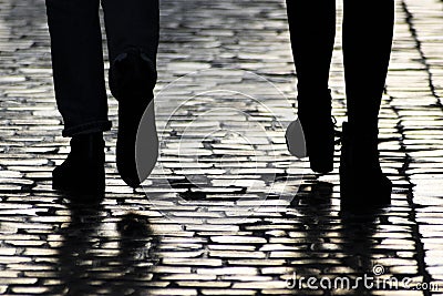 Dark silhouettes and shadows of people on sidewalk. Two pedestrians walking down on evening street. Stock Photo