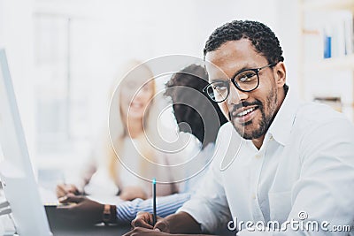 Dark skinned entrepreneur wearing glasses, working in modern office.African american man in white shirt looking and smiling at the Stock Photo