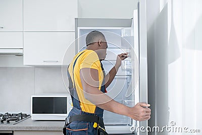 Dark-skinned service man in yellow tshirt standing near the fridge Stock Photo