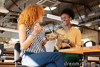 Dark-skinned woman laughing while eating lunch with friend Stock Photo