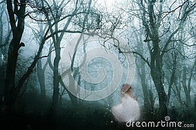 A dark, spooky forest with a ghostly womanin a white dress, on a cold foggy winters day. With an old artistic vintage edit Stock Photo