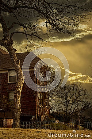 Dark spooky two story brick house with stark winter tree overhanging under ominous sky and strange late day light Stock Photo