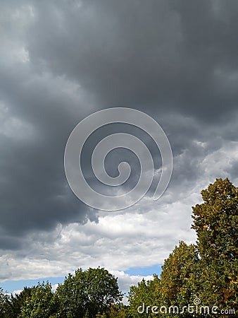 dark storm clouds swirl over the trees in the city center. Clouds in the sky. Stock Photo