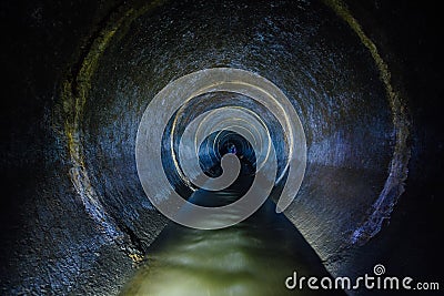 Dark underground sewer round concrete tunnel. Industrial wastewater and urban sewage flowing throw sewer pipe Stock Photo