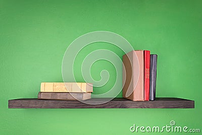 A dark wooden shelf on the green wall, two books are on it and three books are standing vertically Stock Photo