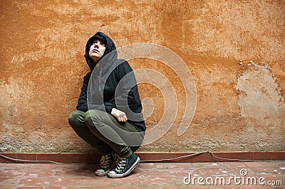 Dark young woman sad crouched near urban wall portrait Stock Photo