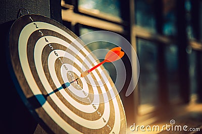Dart arrow hit on bulleyes of dartboard to represent that the business reached the target with dark tone picture style. Target Stock Photo