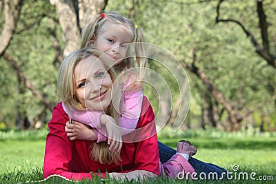 Daughter embraces mother lying on grass Stock Photo