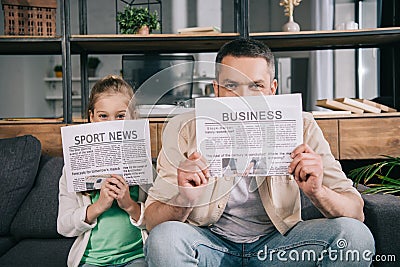 Daughter and father covering faces with business and sport news newspapers Stock Photo