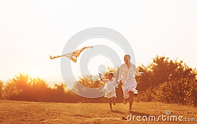 Daughter with her mother have fun together by running with kite on the field. Illuminated by beautiful sunlight Stock Photo