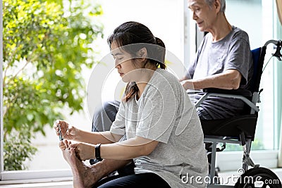 Daughter hold a nail clipper,cutting the ingrown nail for disabled senior mother in wheelchair,asian woman help to cut the toe Stock Photo