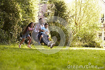 Daughter Pushing Father And Son On Tire Swing In Garden Stock Photo
