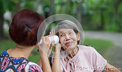 Daughter talking to hearing impaired elderly woman , using paper tube Stock Photo