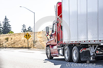 Day cab model red big rig semi truck with roof spoiler transporting cargo in dry van semi trailer running on the highway road with Stock Photo