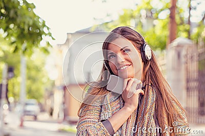 Daydreaming woman listening to the music on a smart phone walking down the street on an autumn sunny day Stock Photo