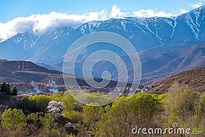 Daytime wide angle shot of Beautiful landscape of snow capped mountains and bushes and a village in the valley. Atlas, Morocco Stock Photo