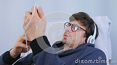 De mens luistert muziek in hoofdtelefoons op smartphone en zingt een lied in karaoke Ontspan tijd na het werk stock videobeelden De mens luistert muziek in hoofdtelefoons op smartphone en zingt een lied in karaoke Ontspan tijd na het werk stock videobeelden